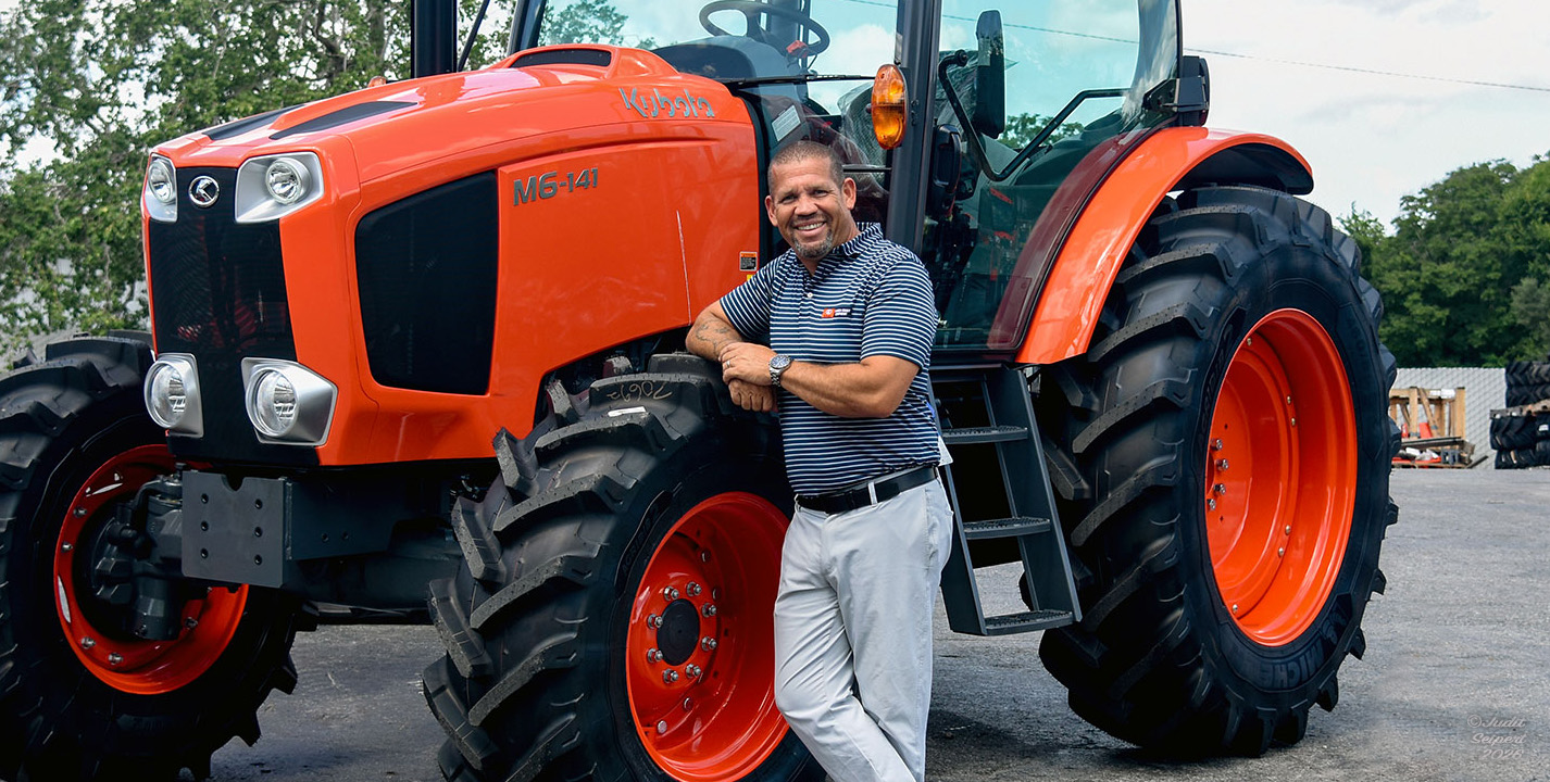 Isaiah Webb, general manager of Florida Coast Equipment’s Ocala Kubota dealership, leans against the tire of an orange Kubota tractor. (Photo: ©Judit Seipert)