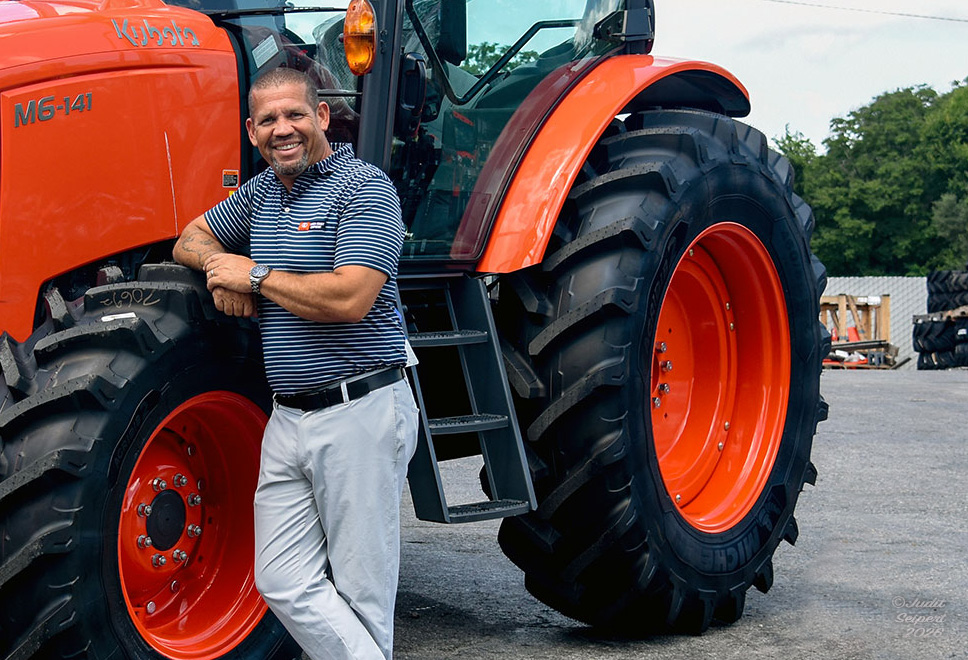 Isaiah Webb, general manager of Florida Coast Equipment’s Ocala Kubota dealership, leans against the tire of an orange Kubota tractor. (Photo: ©Judit Seipert)