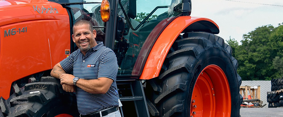 Isaiah Webb, general manager of Florida Coast Equipment’s Ocala Kubota dealership, leans against the tire of an orange Kubota tractor. (Photo: ©Judit Seipert)