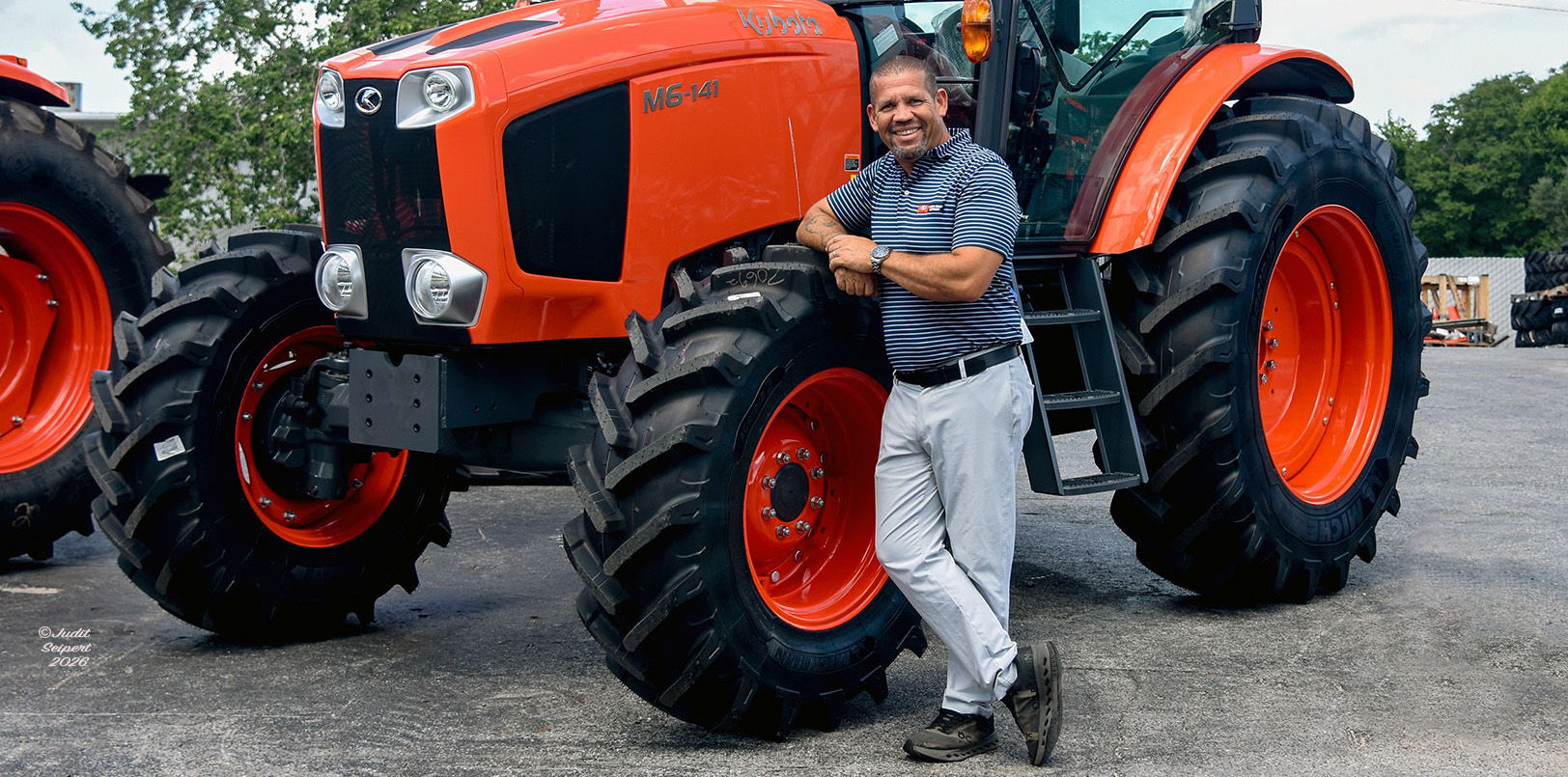 Isaiah Webb, general manager of Florida Coast Equipment’s Ocala Kubota dealership, leans against the tire of an orange Kubota tractor. (Photo: ©Judit Seipert)