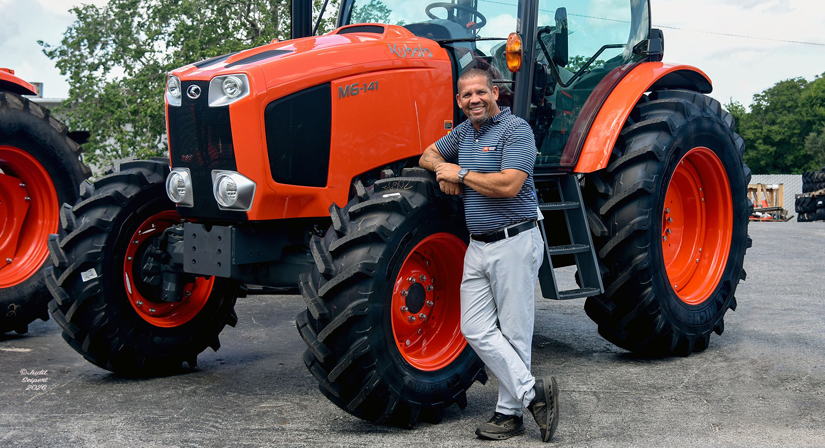 Isaiah Webb, general manager of Florida Coast Equipment’s Ocala Kubota dealership, leans against the tire of an orange Kubota tractor. (Photo: ©Judit Seipert)