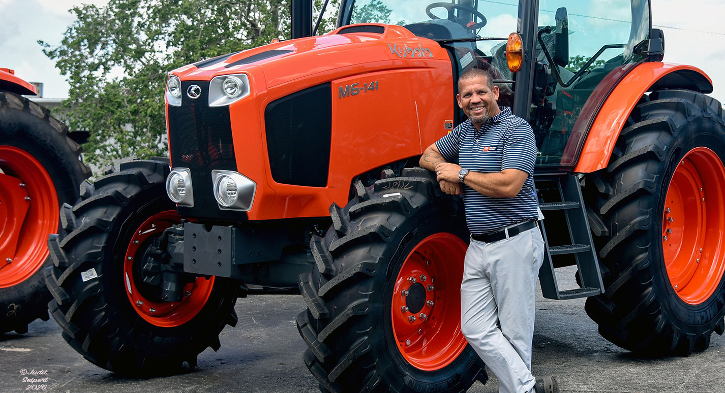 Isaiah Webb, general manager of Florida Coast Equipment’s Ocala Kubota dealership, leans against the tire of an orange Kubota tractor. (Photo: ©Judit Seipert)
