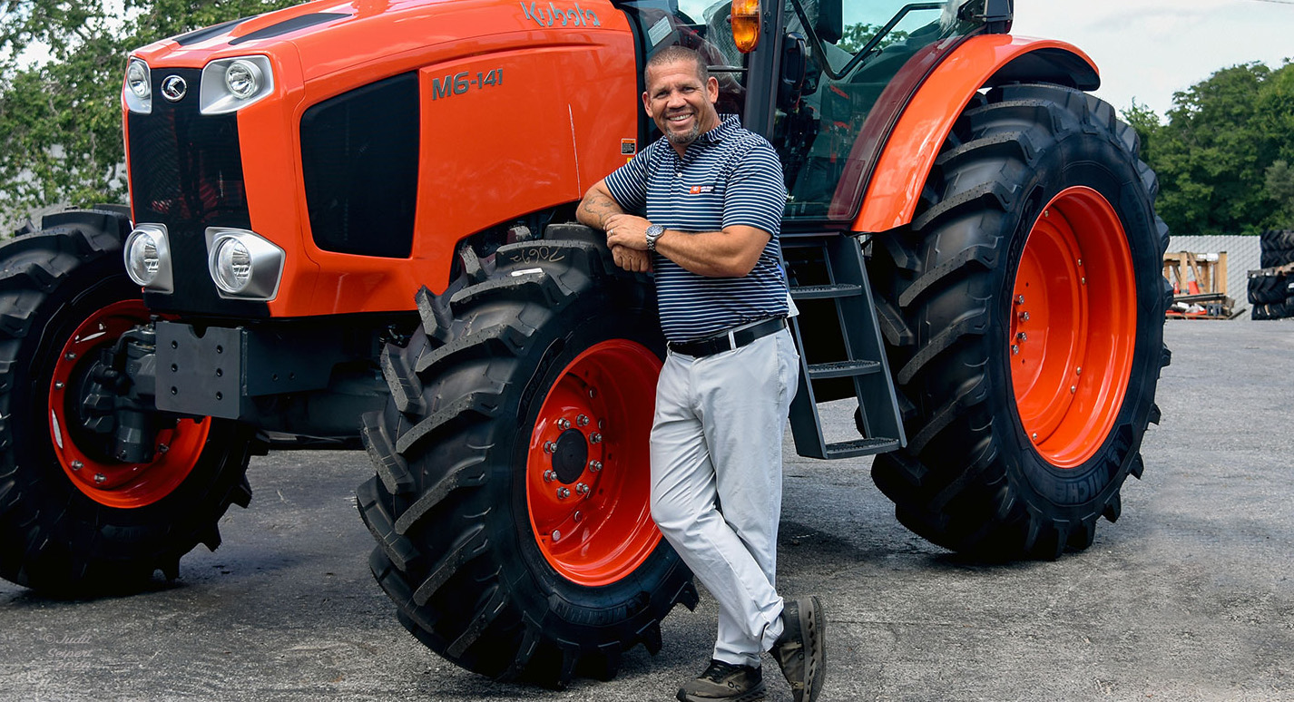 Isaiah Webb, general manager of Florida Coast Equipment’s Ocala Kubota dealership, leans against the tire of an orange Kubota tractor. (Photo: ©Judit Seipert)