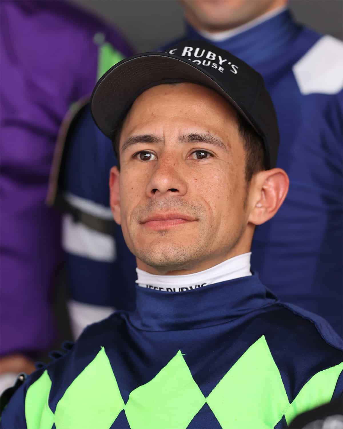 Headshot of jockey Junior Alvarado, wearing deep navy silks with bright green diamonds across the chest. (Photo: ©Renee Torbit/Coady Media)