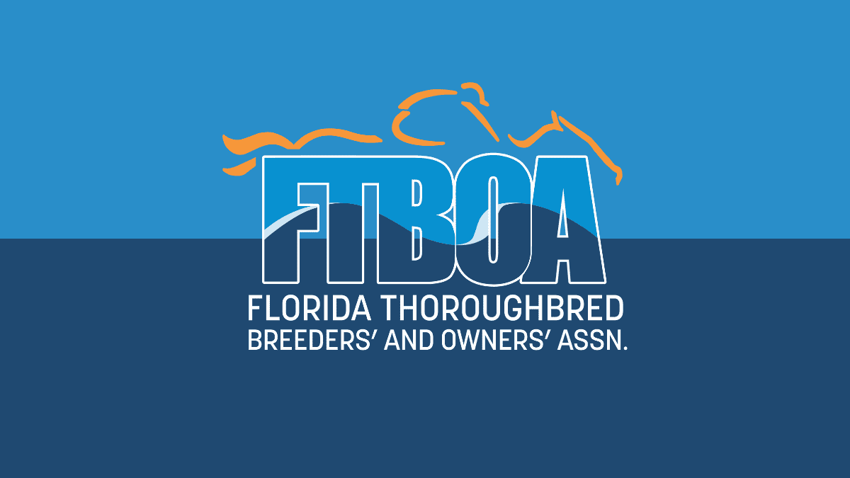 Logo for FTBOA (Florida Thoroughbred Breeders’ and Owners’ Association). The logo is centered on a rectangle background, split in half by light blue (top half) and dark blue (bottom half). The logo itself consists predominantly of large, sans serif letters outlined in white. A wave runs through them, syncing up with the light and blue of the background. Beneath the letters, the full name of the organization is stacked in two rows, with “Association” abbreviated to “Assn.” An orange topline of a horse and jockey race along the top of “FTBOA.”