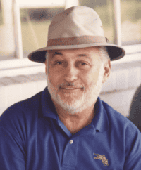Headshot of trainer Stanley M. Ersoff. He’s seated, smiling for the camera, wearing a blue polo collared shirt and khaki-colored fedora.
