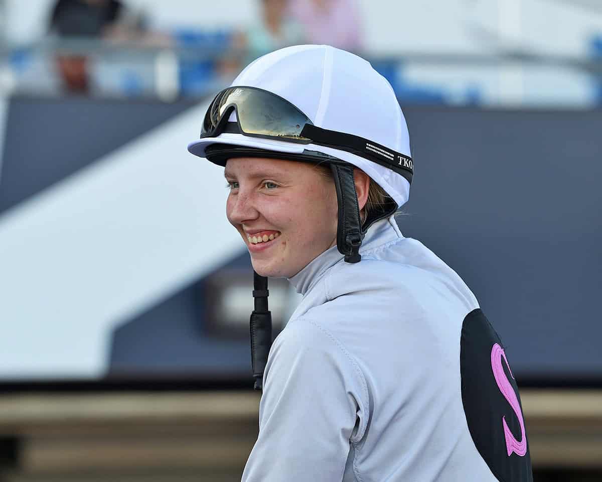 Closely cropped photo of jockey Cornelia Hartsmar, smiling from horseback while turning in the direction of the camera. (Photo: ©Ryan Thompson)