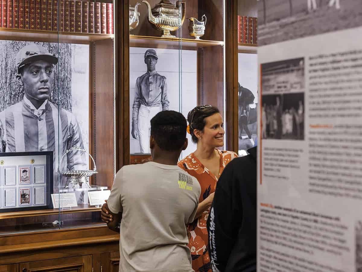 Onlookers walk through the traveling exhibition of The Heart of the Turf: Racing’s Black Pioneers. The exhibition showcases historical imagery, items, and information that explores African American history in Thoroughbred racing and examines how generations of Black professionals shaped the United States racing industry while facing systemic exclusion. (Photo: ©Roda Ferraro)