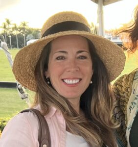 Headshot of Alex Roman posing for a photo with a group (out of frame), wearing a sunhat on a sunny day.