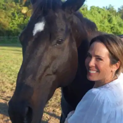 Headshot of Alex Roman hugging her horse, Voo, as she turns to smile at the camera. 