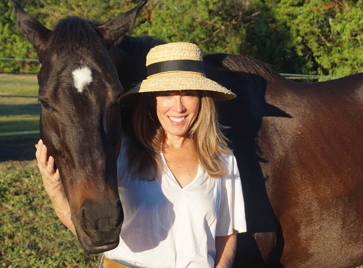Alex Roman, the visionary behind Horse World Advertising & Sponsorships, stands in a sunny pasture with her horse, Voo, as they pose for a photo.