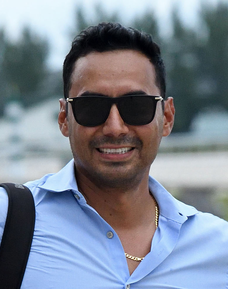 Thoroughbred trainer Carlos David poses for a photo trackside, smiling for the camera while wearing sunglasses. (Photo: ©Ryan Thompson)