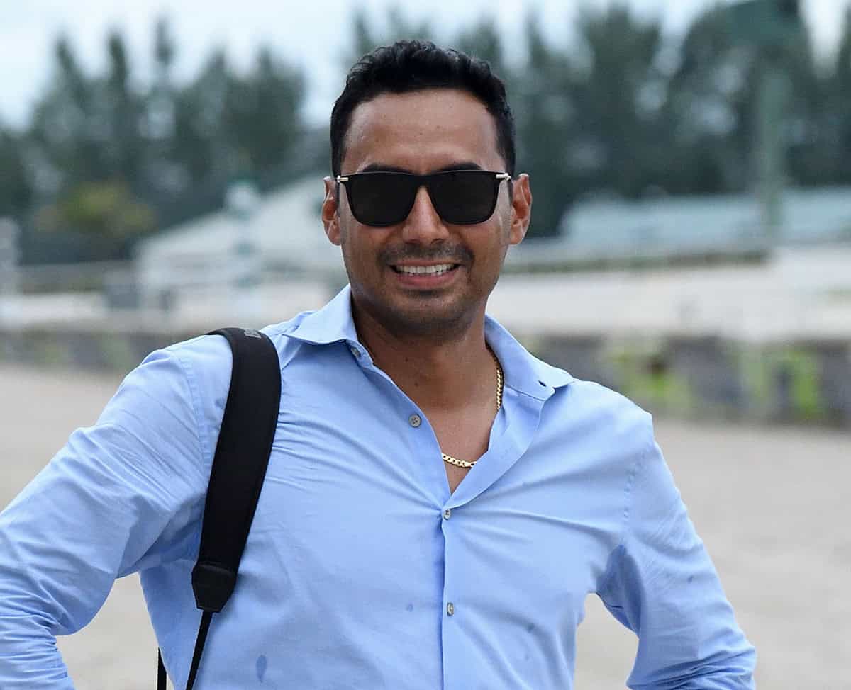 Thoroughbred trainer Carlos David poses for a photo trackside, smiling for the camera while wearing sunglasses. (Photo: ©Ryan Thompson)