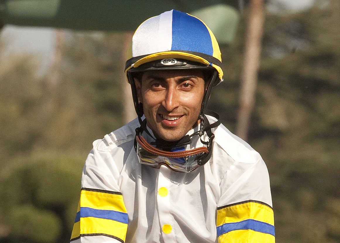 Headshot of Jockey Edwin Maldonado smiles for the camera as he guides the horse he’s riding (out of frame) off the track post-race. (Photo: ©Benoit)