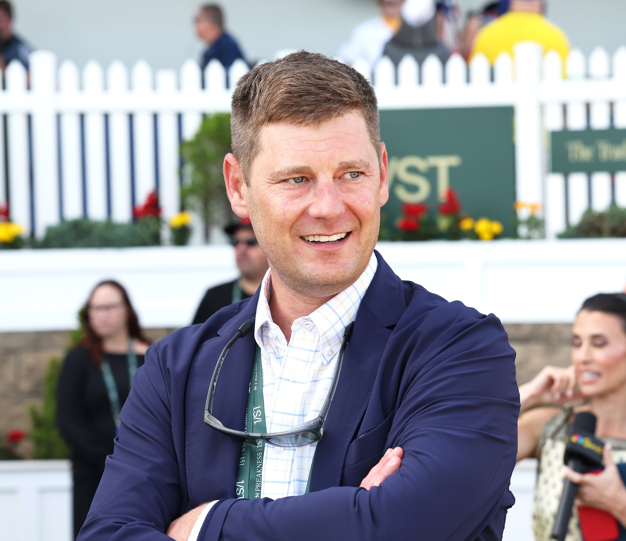 Racehorse trainer J. Kent Sweezey stands trackside with his arms crossed, smiling as he looks toward one of the horses he is training. (Photo: ©Bill Denver/EQUI-PHOTO)