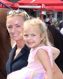 Trainer Saffie Joseph Jr.’s longtime assistant, Sabine Langvad, smiles for the camera from the winner’s circle, holding her daughter Savannah, who also smiles for the photo. (Photo: ©Coglianese)