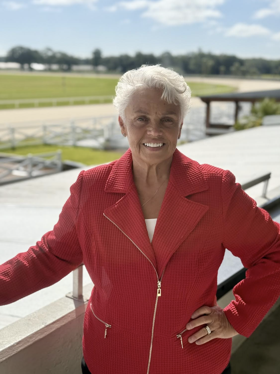Tampa Bay Downs’ Vice President of Marketing and Publicity, Margo Flynn, leans against the railing of the Tampa Bay Downs grandstand, smiling for a photo. (Photo: ©Tampa Bay Downs)