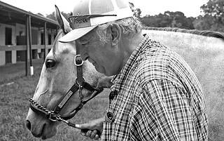 Closely cropped grayscale photo of Max Ubide leading gray Florida-bred Thoroughbred Nina’s Last Gift by the barns on the OBS Sale grounds. (Photo: ©Judit Seipert)