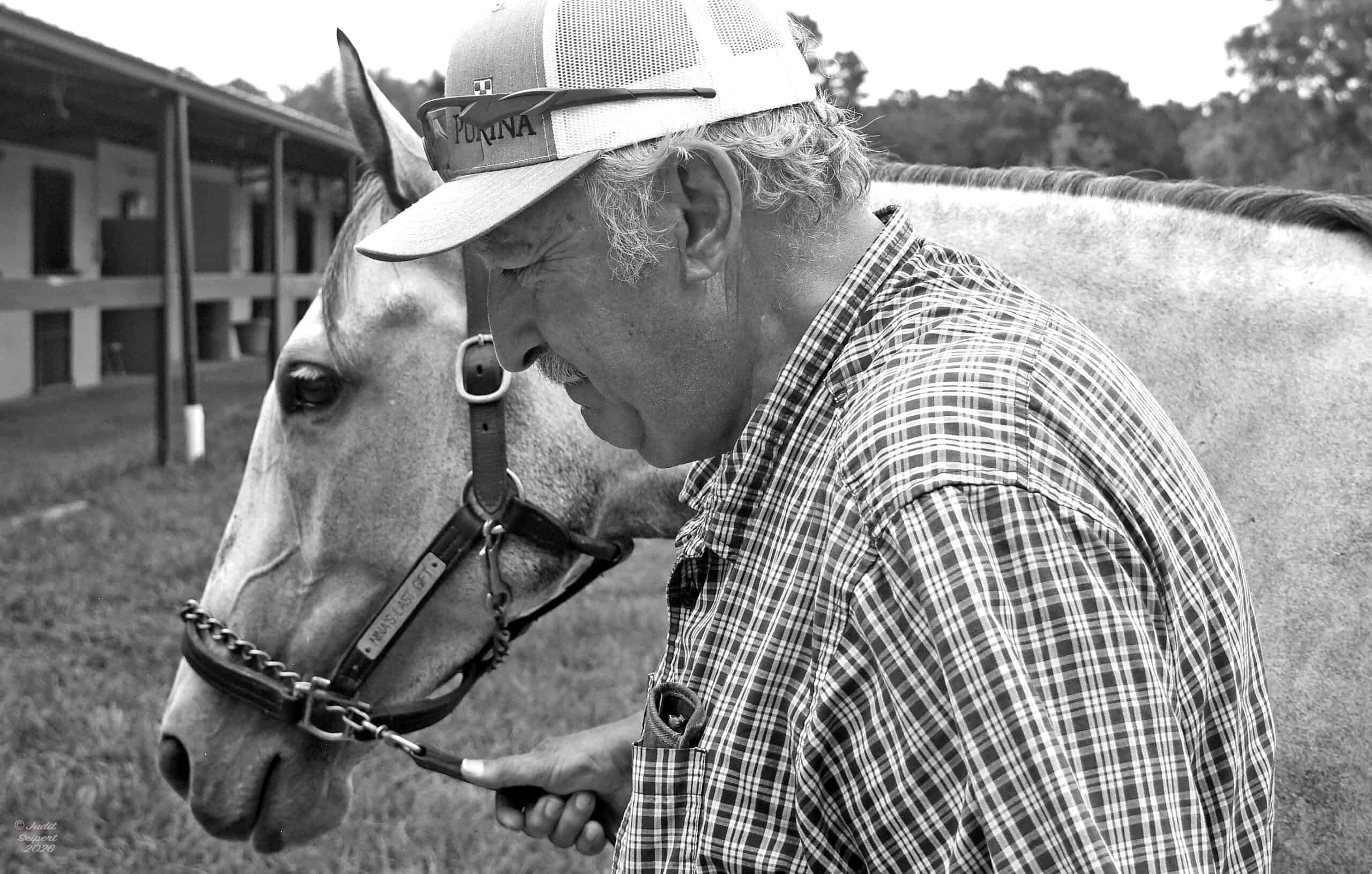 Closely cropped grayscale photo of Max Ubide leading gray Florida-bred Thoroughbred Nina’s Last Gift by the barns on the OBS Sale grounds. (Photo: ©Judit Seipert)