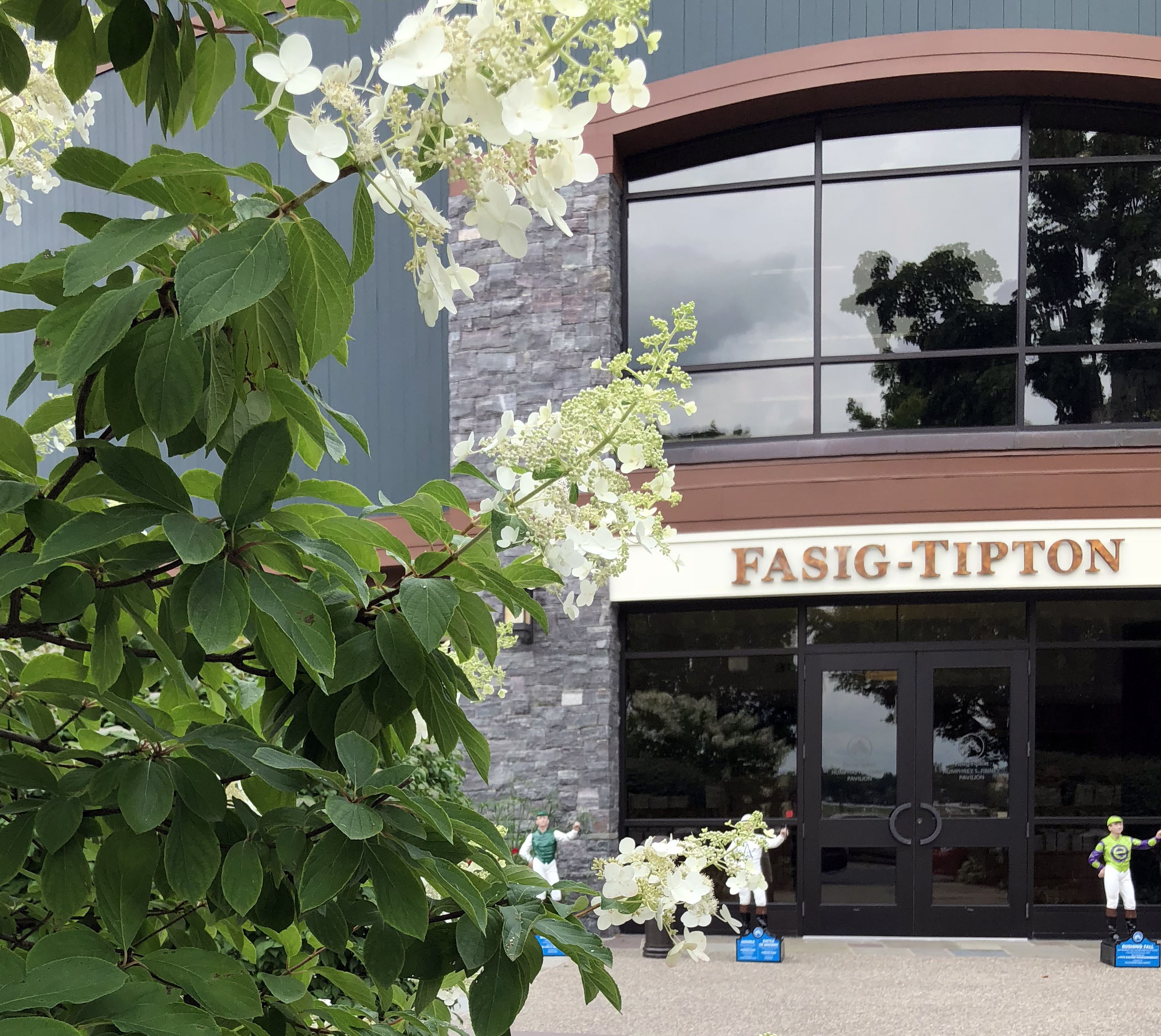 Entrance of the Fasig-Tipton Finney Pavilion. Lawn jockeys stand guard outside the entrance, and blooming flowers frame the left side of the photo. (©Fasig-Tipton Photo)