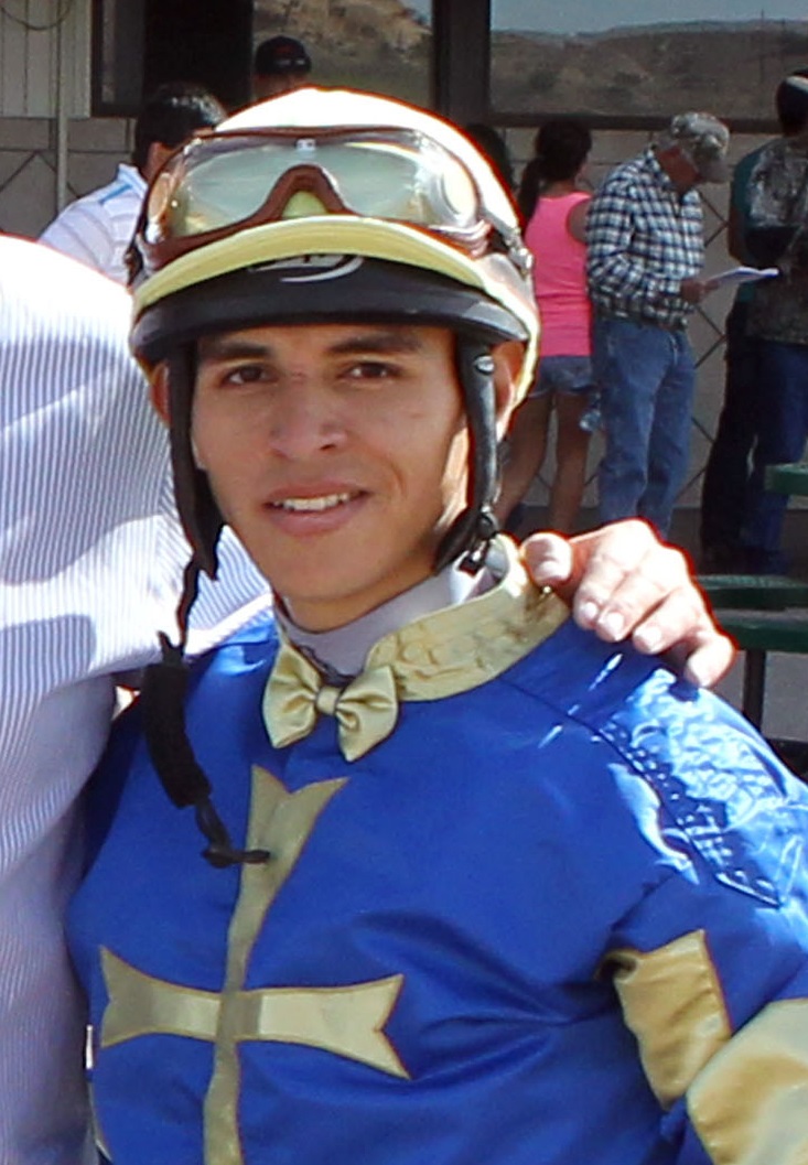Headshot photo of jockey Elvin Gonzalez dressed in blue and yellow silks in the winner’s circle. (Photo: ©Coady)