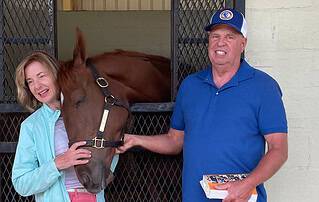 Diane (left) and David (right) Osterholt stand in front of the stall of Giftbox Surprise, a 2022 chestnut Florida-bred Thoroughbred filly they bred by Gift Box and Glenwood Pines, on the OBS Sale Grounds. Giftbox Surprise rubs her head happily against Diane. (Photo Courtesy Diane Osterholt)