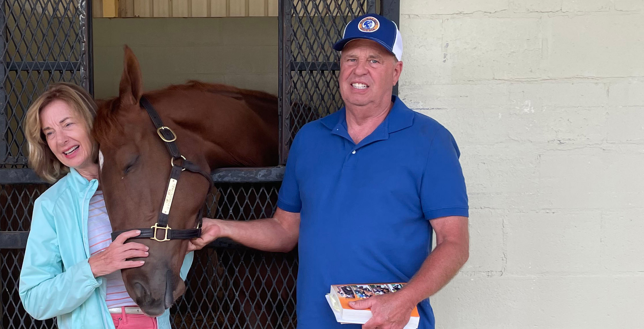Diane (left) and David (right) Osterholt stand in front of the stall of Giftbox Surprise, a 2022 chestnut Florida-bred Thoroughbred filly they bred by Gift Box and Glenwood Pines, on the OBS Sale Grounds. Giftbox Surprise rubs her head happily against Diane. (Photo Courtesy Diane Osterholt)