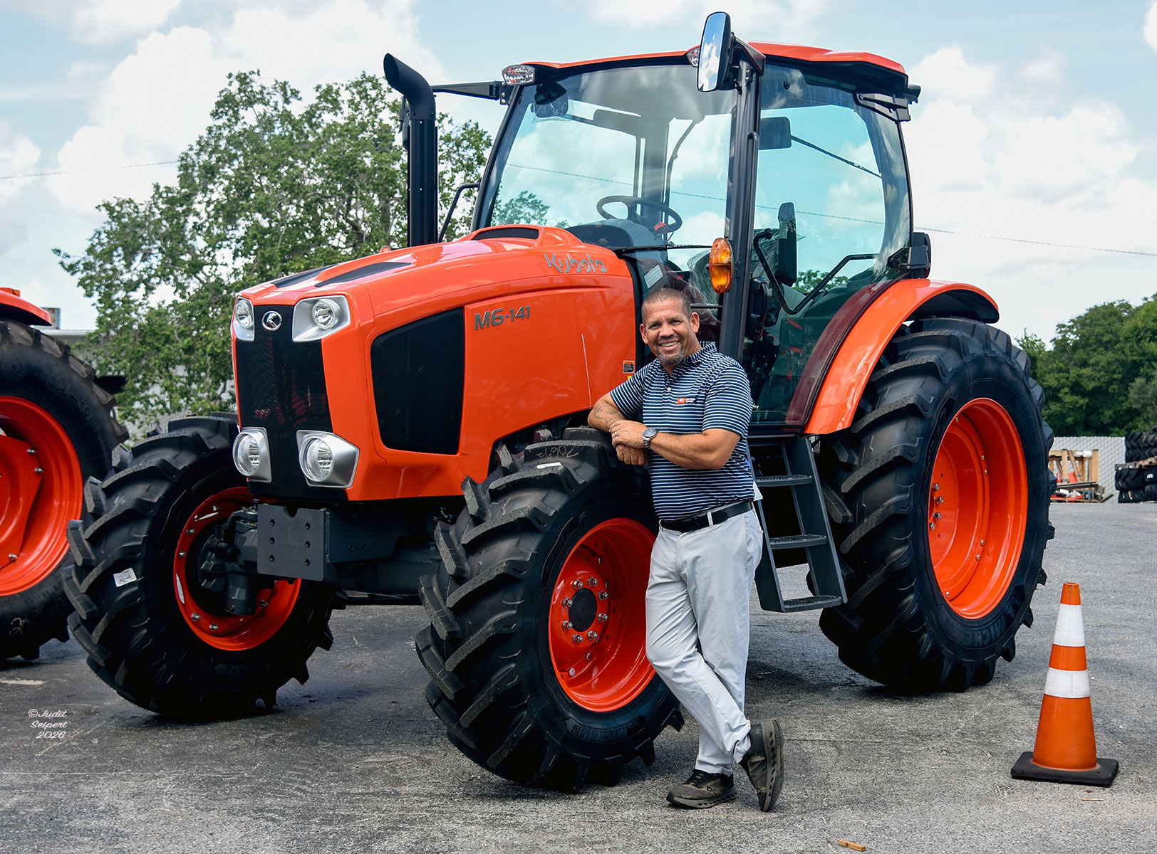 Isaiah Webb, general manager of Florida Coast Equipment’s Ocala Kubota dealership, leans against the tire of an orange Kubota tractor. (Photo: ©Judit Seipert)