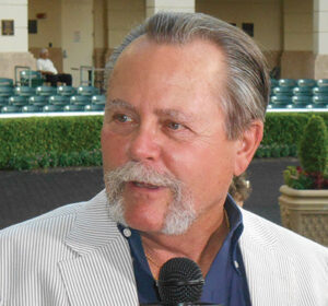Candid headshot of Brent Fernung, who is speaking to someone out of frame while at a Thoroughbred auction. The auction arena stands behind him. 
