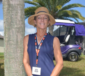 Golf Chair Beth Bayer smiles for a photo on a sunny day next to a palm tree on a golf course.
