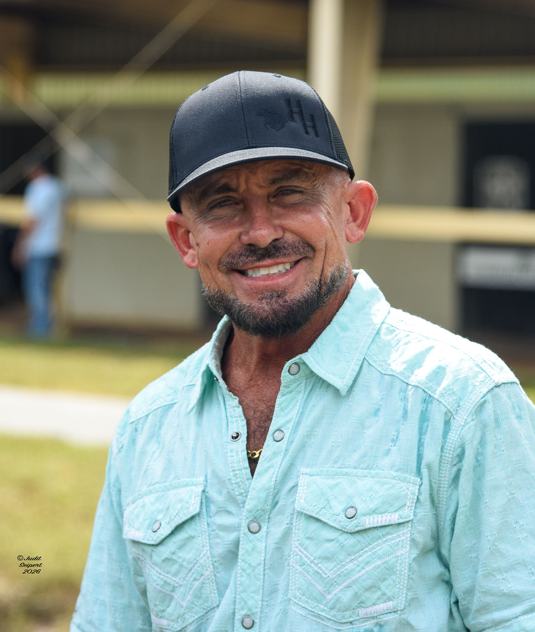 Candid headshot of Hal Hatch smiling at the camera in front of the OBS Sales’ barns. (Photo: ©Judit Seipert)